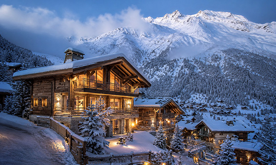 Snow-covered luxury chalet in the French Alps with mountain views and warm lights at dusk